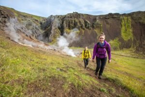 Smiling couple hiking through a geothermal valley in southern Iceland, with steam rising from the earth and dramatic volcanic cliffs in the background—an adventurous and unique honeymoon destination beyond the ordinary.