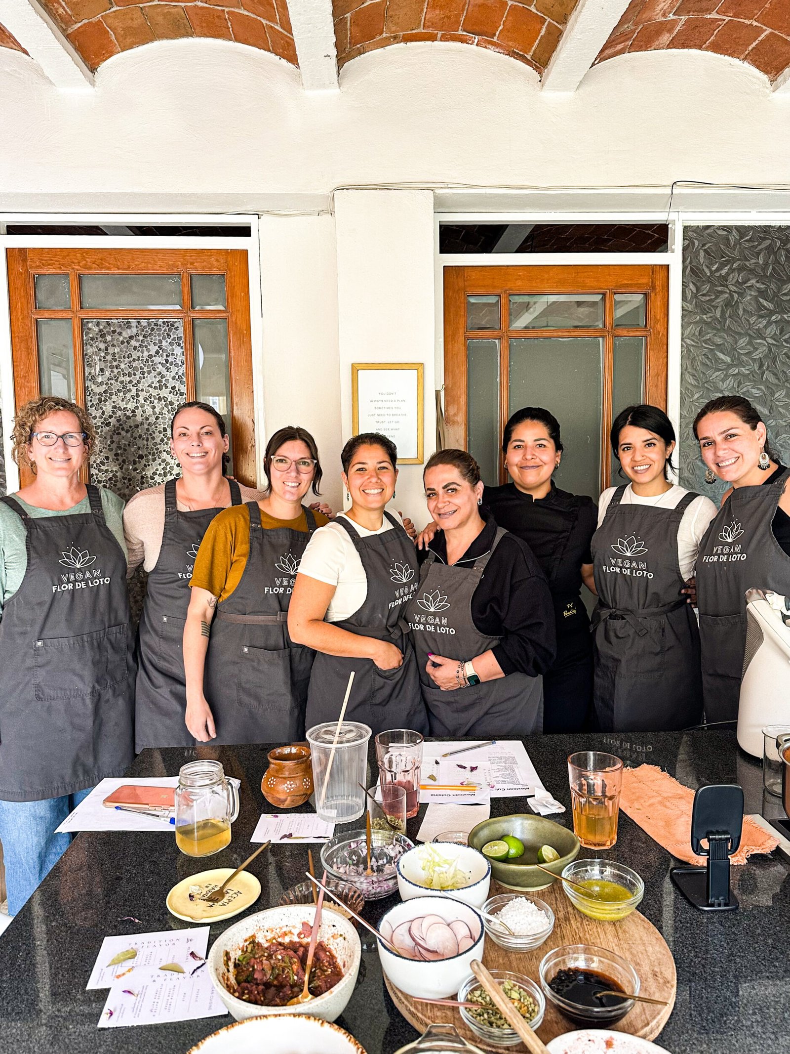 Woman in a traditional apron leading a Mexican cooking class in Mexico City, standing behind a colorful table with traditional dishes and ingredients.