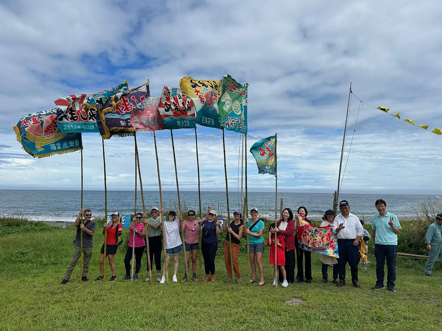 Group of locals and visitors waving colorful traditional flags by the sea in Hirono, Japan, during the Hirono Emotion welcome for the scenic train along the Michinoku Coastal Trail