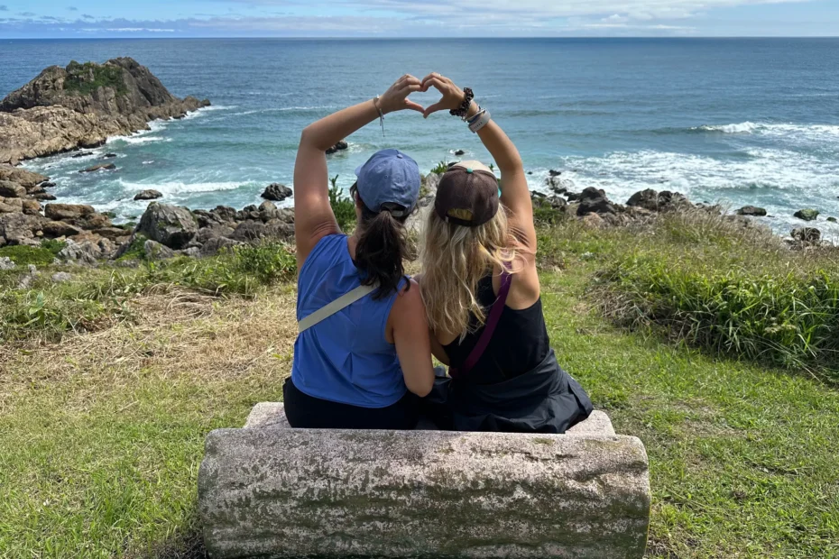 Two friends sitting on a bench forming a heart shape with their hands while overlooking the Pacific Ocean along the Michinoku Coastal Trail in Japan