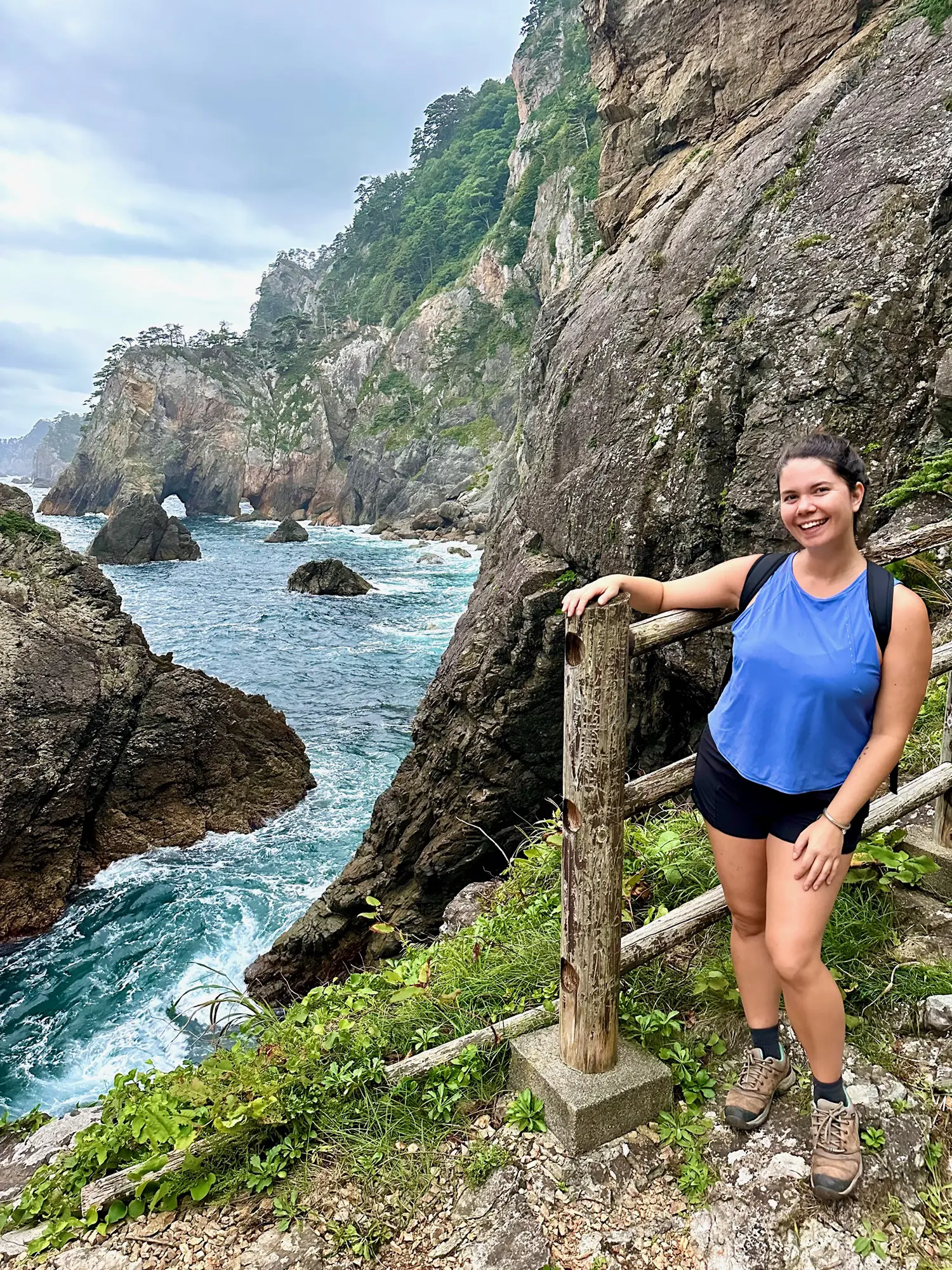 Nicola standing on a cliffside trail overlooking the rocky shoreline of the Michinoku Coastal Trail, symbolizing the resilience taught through the Tendenko philosophy in Japan